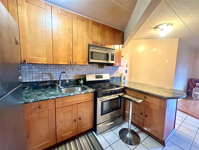 Kitchen featuring stainless steel appliances, a peninsula, decorative backsplash, light tile patterned flooring, and dark stone countertops | Image 4