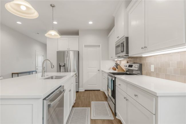Kitchen with appliances with stainless steel finishes, light wood finished floors, tasteful backsplash, white cabinets, and light countertops | Image 5