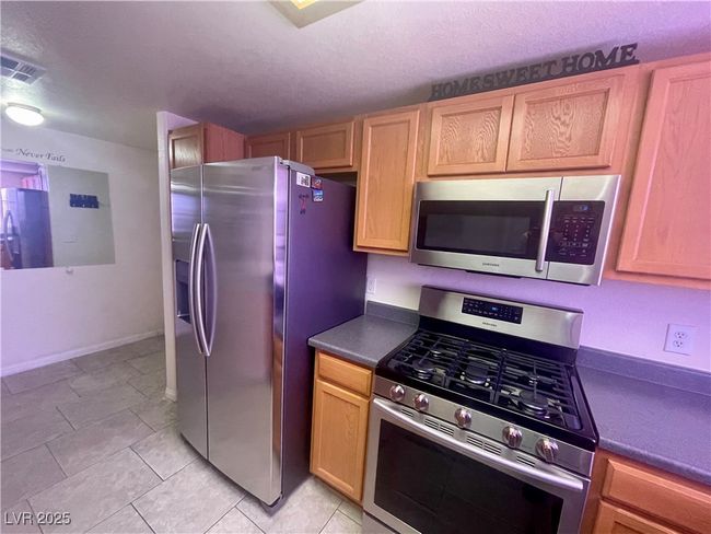 Kitchen featuring a textured ceiling, visible vents, appliances with stainless steel finishes, dark countertops, and baseboards | Image 8