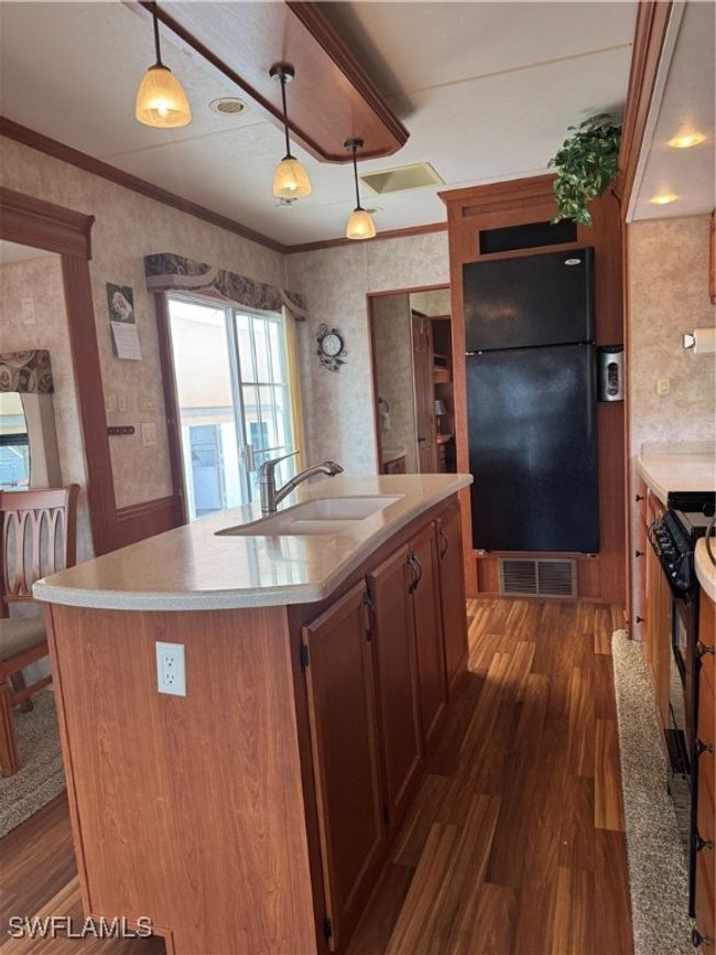 Kitchen featuring an island with sink, hanging light fixtures, sink, ornamental molding, and fridge | Image 31