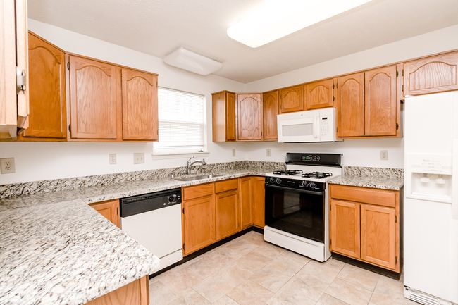 kitchen featuring light stone counters, a sink, and white appliances | Image 11