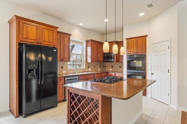 Kitchen with black appliances, brown cabinetry, a kitchen island, dark stone countertops, and decorative backsplash | Image 14