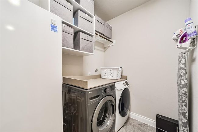 This laundry room is spacious enough for a full sized refrigerator and washer/dryer. Ample shelving with storage bins, and a neat ironing area, offering efficient organization in a compact space. | Image 22