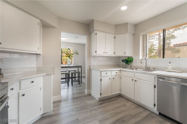 Kitchen featuring dishwasher, backsplash, white cabinetry, light wood-style flooring, and light countertops | Image 11