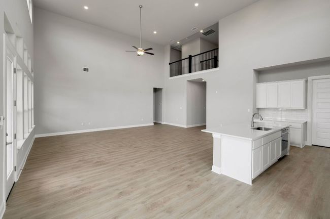 Kitchen with ceiling fan, open floor plan, light countertops, light wood-style flooring, and a towering ceiling | Image 6