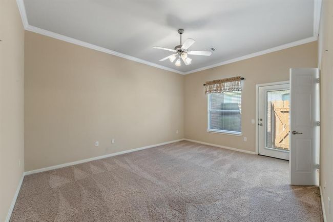 The spacious secondary bedroom boasts carpeted floors, crown molding, and ceiling fans for comfort and style. It offers a bright, inviting space ideal for family or guests. There is also a charming exterior door to a small patio next to a gate to backyard. | Image 15
