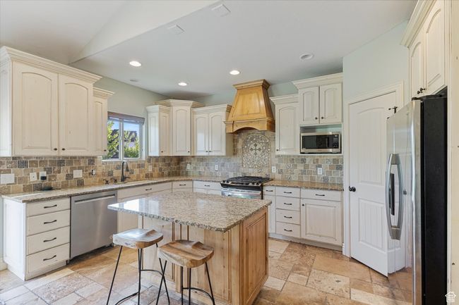 Kitchen with appliances with stainless steel finishes, premium range hood, a sink, backsplash, and light stone countertops | Image 5