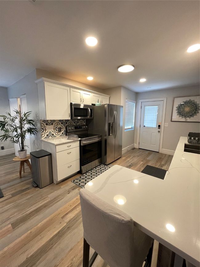 Kitchen featuring white cabinetry, appliances with stainless steel finishes, light wood-style flooring, recessed lighting, and a peninsula | Image 6
