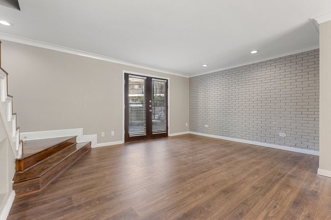 Unfurnished room with crown molding, brick wall, stairs, french doors, and dark wood-style floors | Image 5