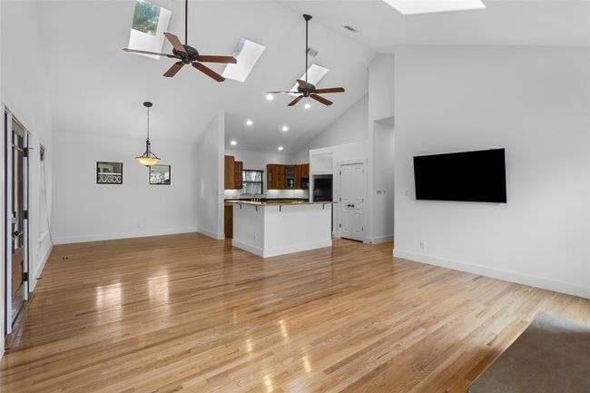 Unfurnished living room featuring light wood-style floors, a skylight, high vaulted ceiling, and a ceiling fan | Image 6