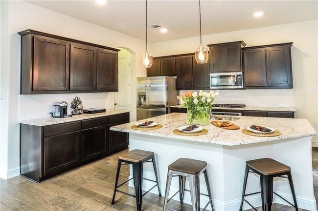 Kitchen with stainless steel appliances, a kitchen breakfast bar, light wood finished floors, dark brown cabinets, and recessed lighting | Image 10