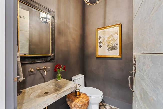 The powder room is located on the first floor between the guest suite and mudroom. Exquisitely plastered in a rustic tone, the space features a reclaimed stone trough as a wash basin and wall mounted Kohler faucet fixtures. Not to be missed is the antique wood door that has been retrofitted for this exact space. | Image 15