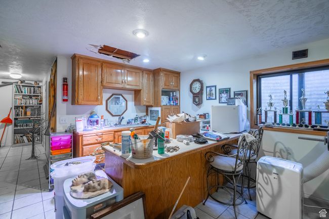 Kitchen with light tile patterned floors, light countertops, a breakfast bar, a desk, and recessed lighting | Image 46
