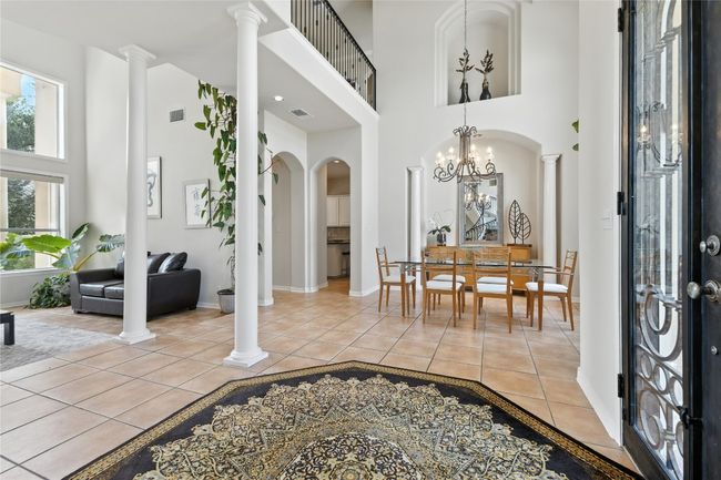 Entrance foyer with a high ceiling, ornate columns, arched walkways, light tile patterned floors, and a chandelier | Image 12