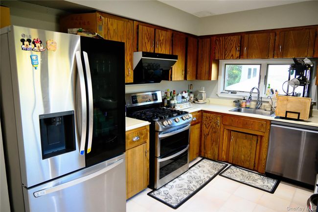 Kitchen featuring stainless steel appliances, light countertops, brown cabinets, extractor fan, and light tile patterned floors | Image 15