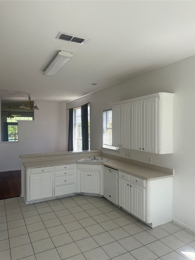Kitchen with a peninsula, visible vents, white cabinetry, dishwashing machine, and light countertops | Image 10