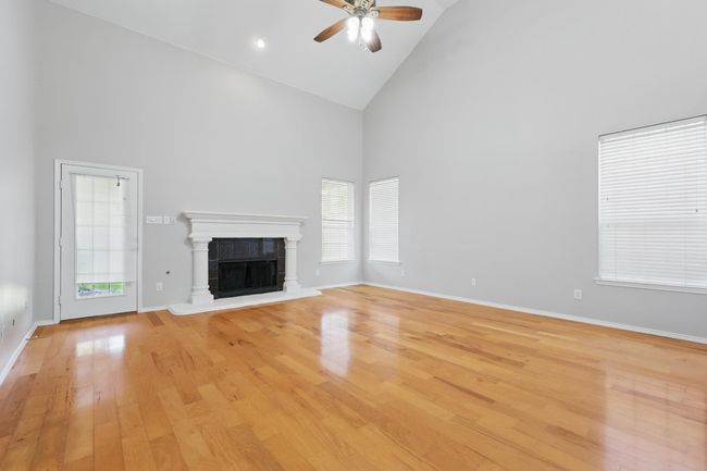 Unfurnished living room with high vaulted ceiling, a ceiling fan, healthy amount of natural light, light wood-style floors, and a tiled fireplace | Image 6