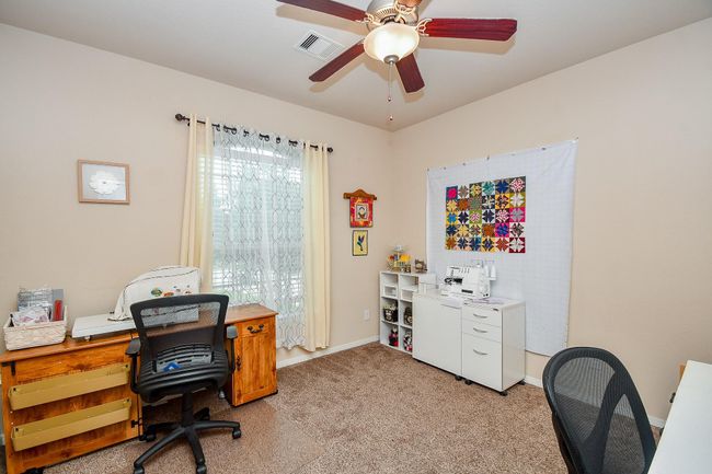 Cozy home office or craft room featuring carpeted flooring, a ceiling fan, and natural light from a window with sheer curtains. | Image 22