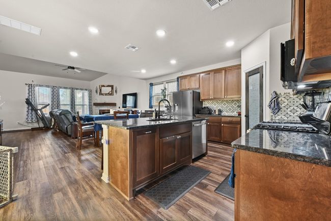 Kitchen featuring stainless steel appliances, dark wood-style floors, ceiling fan, backsplash, and granite counters | Image 6