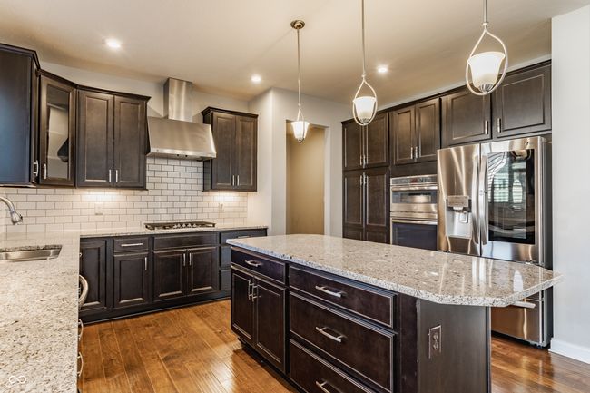 kitchen featuring dark wood finished floors, stainless steel appliances, a sink, wall chimney exhaust hood, and dark brown cabinetry | Image 20