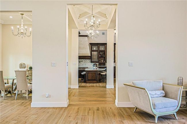 Corridor featuring a chandelier, light wood-style floors, crown molding, coffered ceiling, and beam ceiling | Image 23