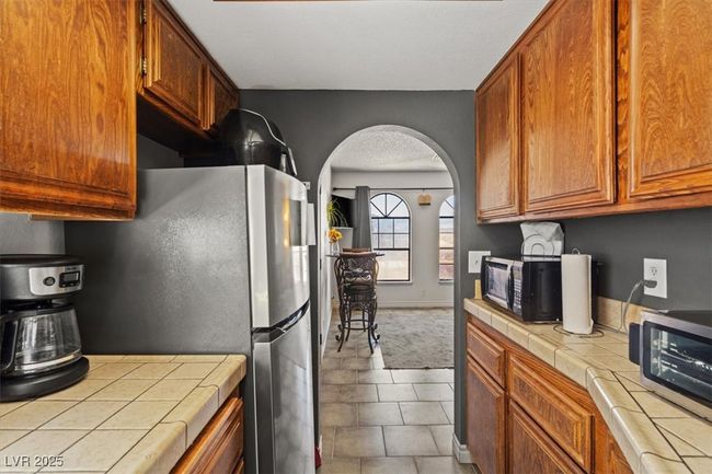 Kitchen featuring brown cabinetry, freestanding refrigerator, black microwave, tile counters, and arched walkways | Image 35