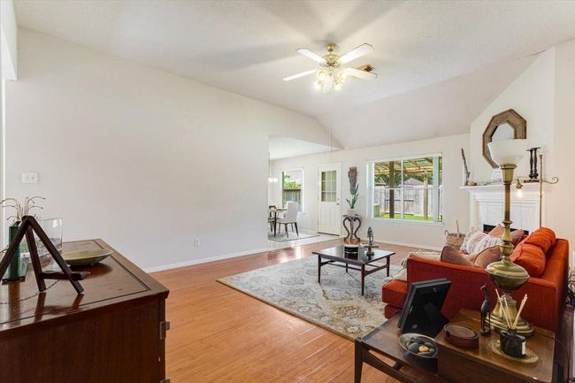 Another angle of the living room featuring an open layout with warm laminate flooring, a cozy fireplace, and ample natural light from large windows. | Image 9