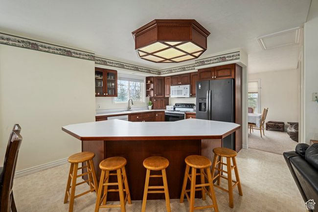 Kitchen with electric range oven, light countertops, a breakfast bar area, white microwave, and glass insert cabinets | Image 19