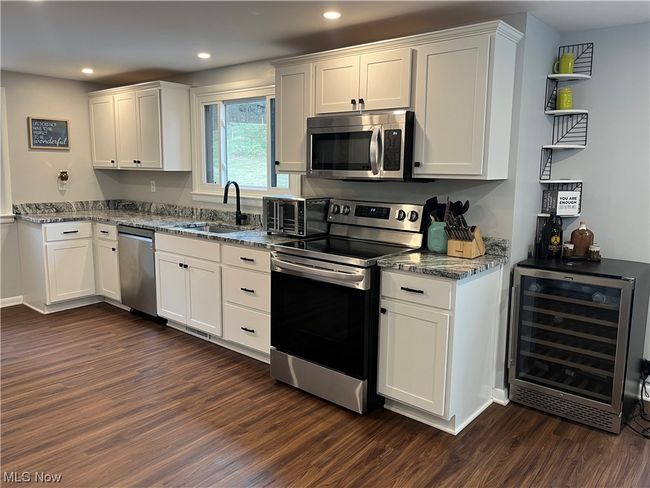 Kitchen featuring dark hardwood / wood-style floors, appliances with stainless steel finishes, beverage cooler, and white cabinetry | Image 12