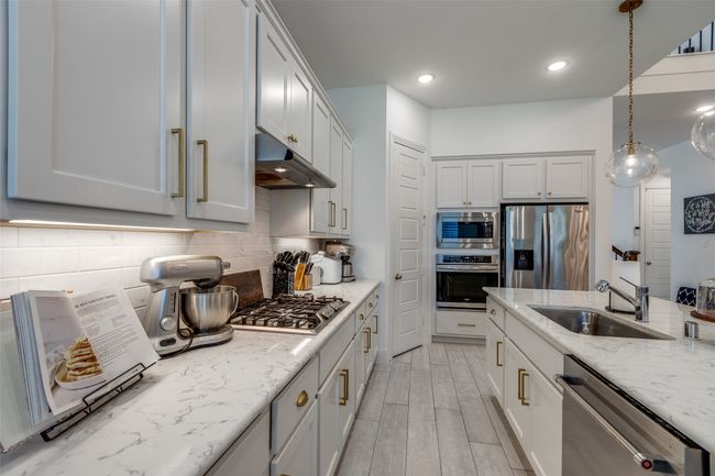 Kitchen with a sink, decorative backsplash, light stone counters, under cabinet range hood, and appliances with stainless steel finishes | Image 20