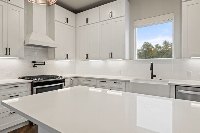 Kitchen with range hood, decorative backsplash, sink, stainless steel appliances, and white cabinets, pot filler | Image 12