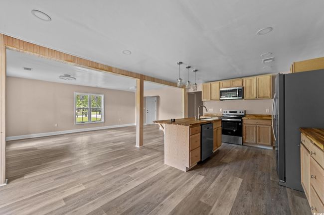 Kitchen featuring open floor plan, stainless steel appliances, an island with sink, wood finished floors, and light brown cabinets | Image 23