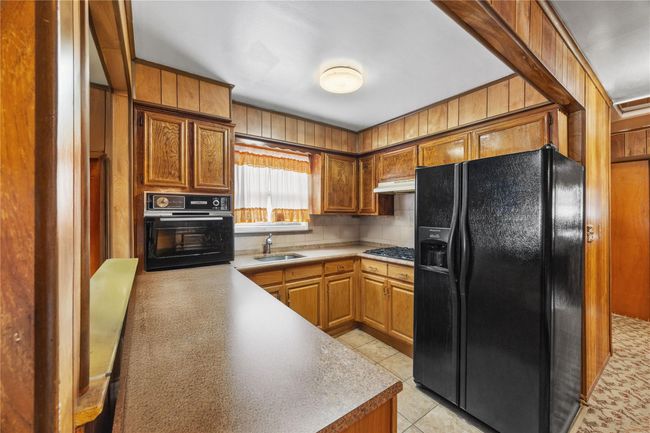 Kitchen featuring black appliances, backsplash, light tile patterned flooring, light countertops, and brown cabinetry | Image 13
