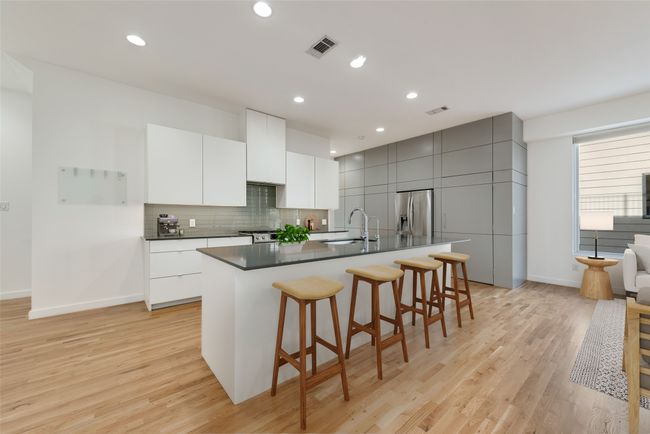 Kitchen featuring stainless steel refrigerator with ice dispenser, a breakfast bar area, dark countertops, a sink, and light wood flooring | Image 5