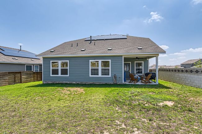 Rear view of house featuring ceiling fan, a patio area, a fenced backyard, a shingled roof, and solar panels | Image 27