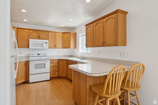 Kitchen featuring white appliances, a peninsula, recessed lighting, light wood-style floors, and light countertops | Image 7