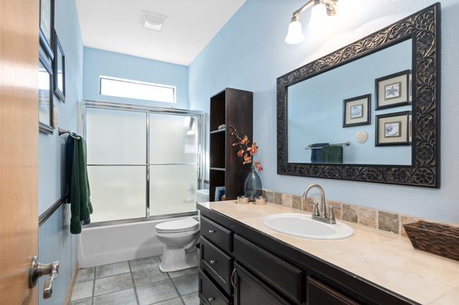 Full bathroom featuring toilet, vanity, tile patterned floors, and shower / bath combination with glass door | Image 21