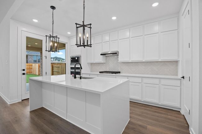 Kitchen featuring a chandelier, appliances with stainless steel finishes, tasteful backsplash, dark wood-type flooring, and under cabinet range hood | Image 6