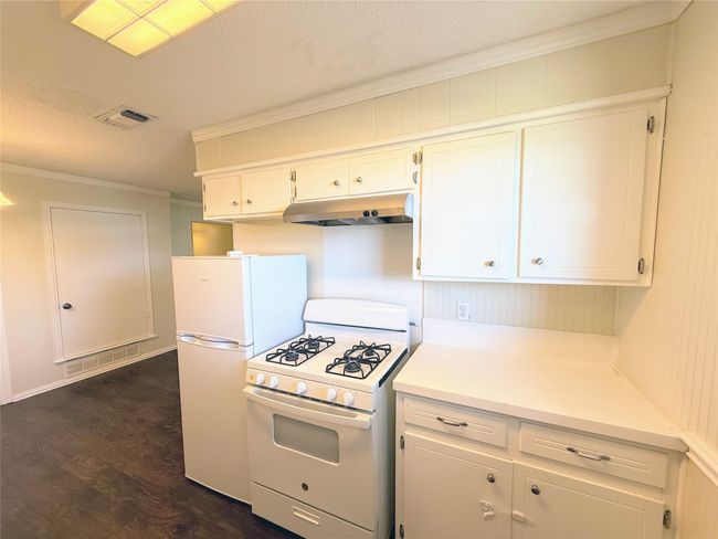 Kitchen featuring white appliances, under cabinet range hood, ornamental molding, a textured ceiling, and white cabinets | Image 9
