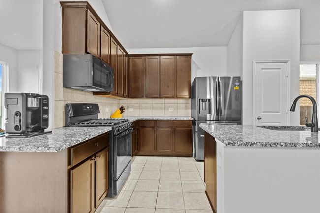 Kitchen featuring black appliances, tasteful backsplash, light tile patterned flooring, a sink, and light stone countertops | Image 17