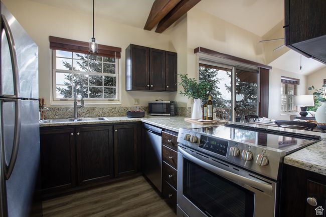 Kitchen featuring appliances with stainless steel finishes, dark wood-style floors, light stone counters, a sink, and hanging light fixtures | Image 6