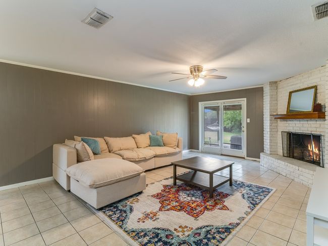 Living room with light tile patterned floors, crown molding, ceiling fan, a brick fireplace, and wooden walls | Image 6