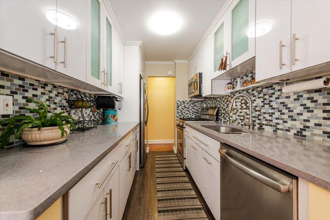 Kitchen with stainless steel appliances, decorative backsplash, dark wood-style floors, glass insert cabinets, and white cabinets | Image 9