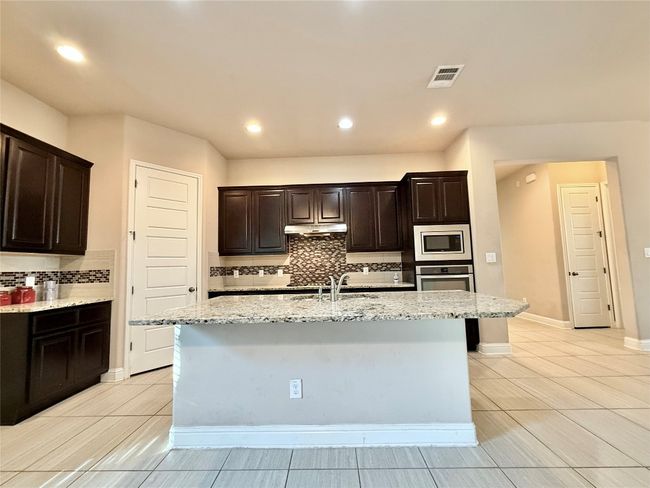 Kitchen featuring backsplash, light stone counters, a kitchen island with sink, and recessed lighting | Image 14