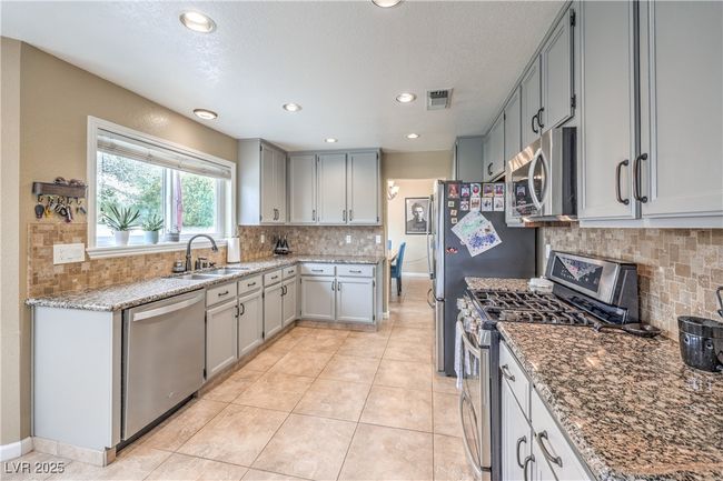 Kitchen with light tile patterned floors, light stone countertops, a sink, and appliances with stainless steel finishes | Image 18