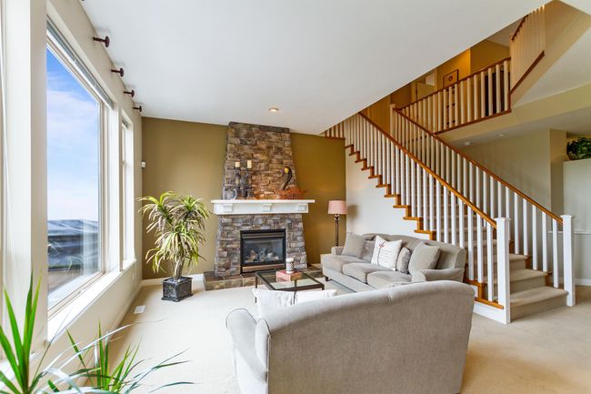 Living area featuring light colored carpet, stairs, a healthy amount of sunlight, and a stone fireplace | Image 7
