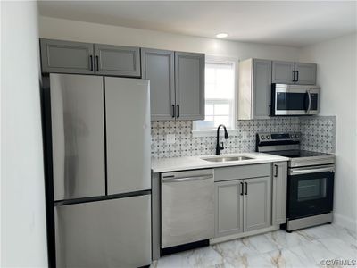 Kitchen with light tile floors, sink, stainless steel appliances, gray cabinets, and backsplash | Image 1