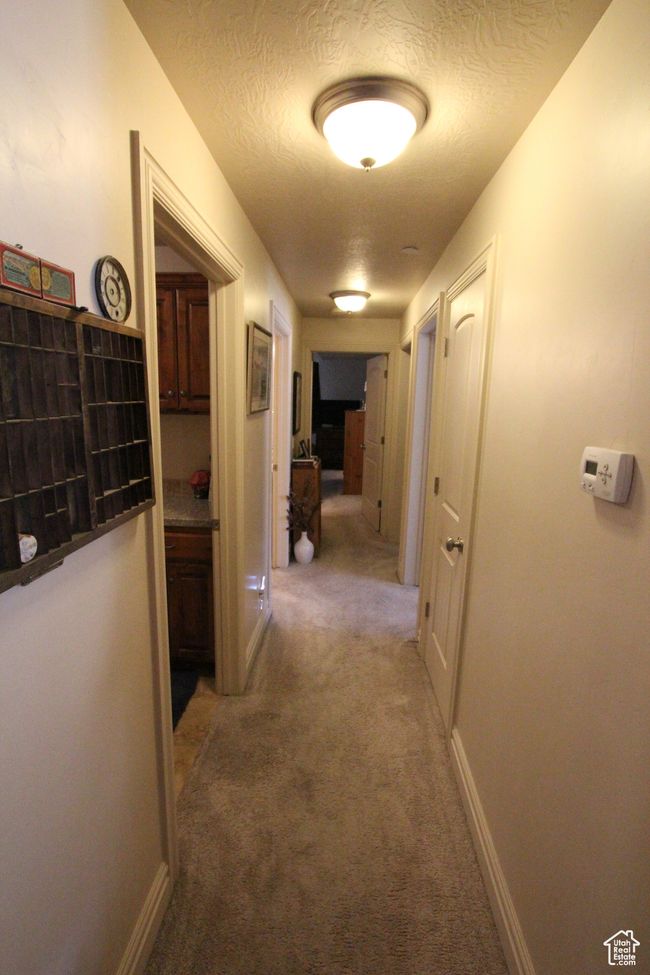 Hallway with light carpet, a textured ceiling, and baseboards | Image 8