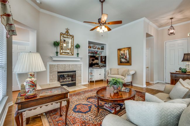 Living room with ornamental molding, wood finished floors, a fireplace, built in features, and a ceiling fan | Image 9