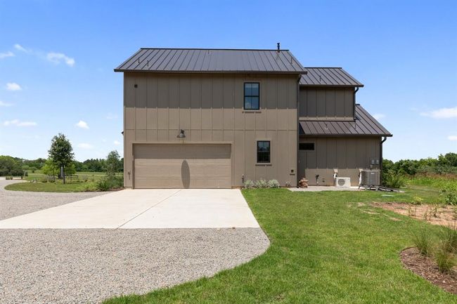 The two car garage is on the side of the house. A concrete pad provides functionality and contrasts the gravel driveway from the road to the garage. | Image 46